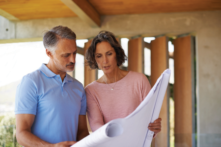A couple in their 50s looking at house plans, while standing under what appears to be a porch.