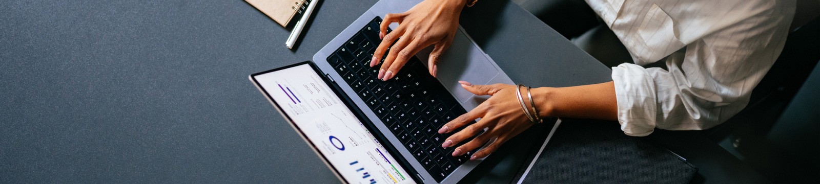 Laptop open on desk with a woman's hands visible typing.  